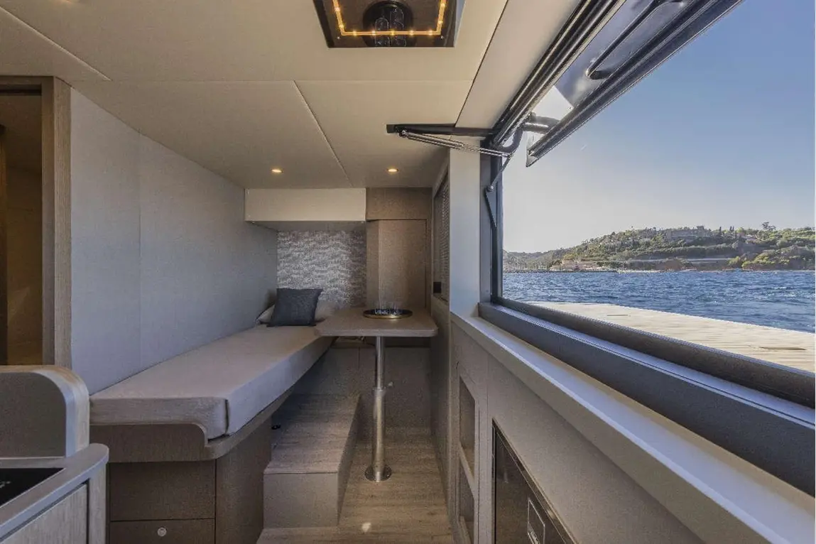 Interior of a modern boat cabin with a sofa, small table, and scenic view of water and hills through large window.